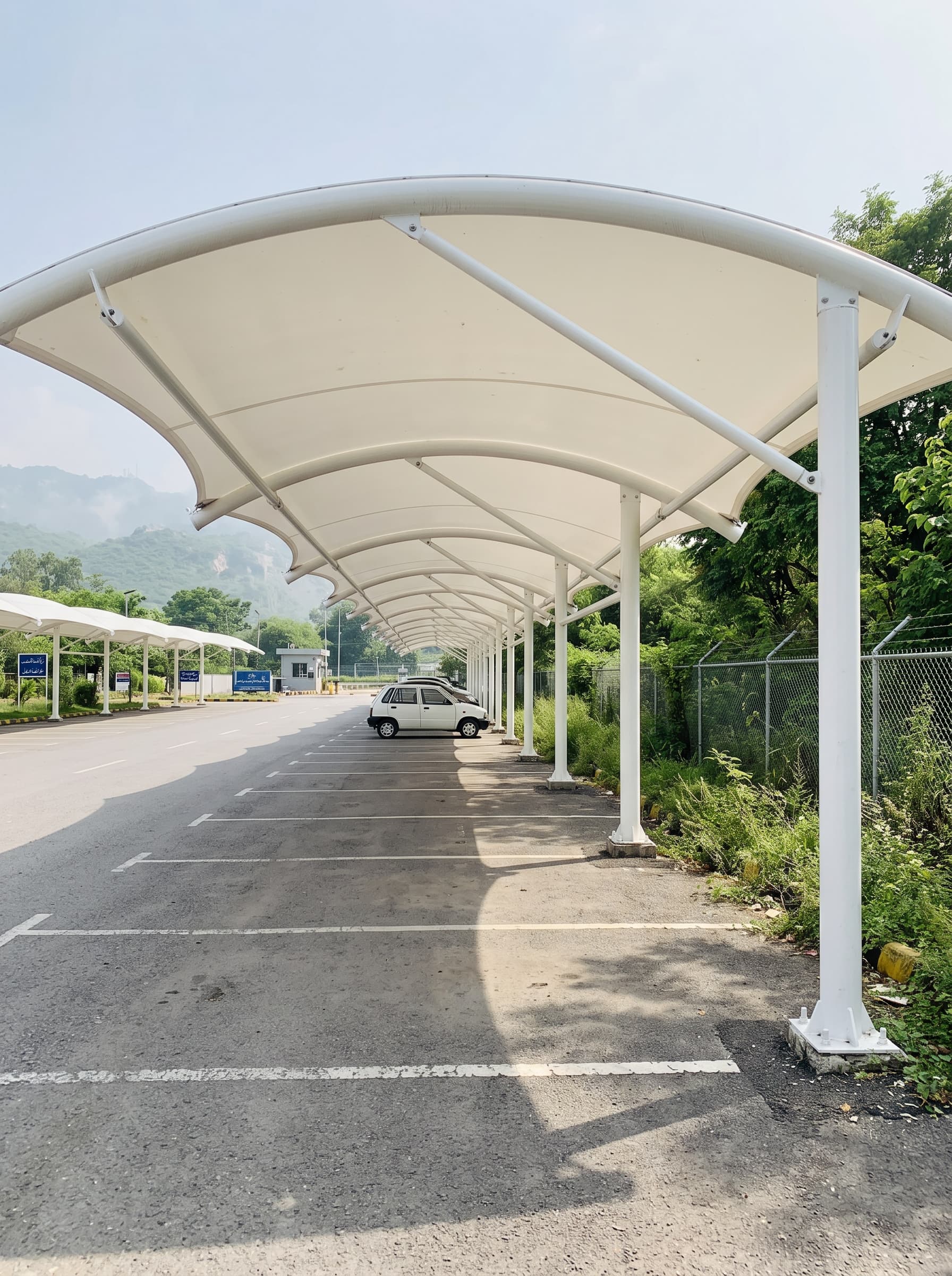 White tensile car parking shades on steel posts along a parking row
